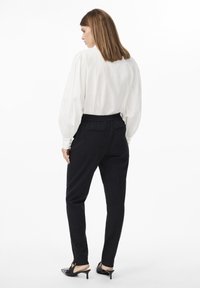 White puff-sleeve blouse with button details, paired with black tapered trousers featuring an elastic waistband and subtle pockets. Black high-heel mules.