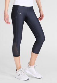Laajakosketuksen tummansiniset capri-leggingsit, joissa on sileä pinta, ja nilkoissa on verkkopaneelit sekä kontrastiväriset ompeleet. Yhdistetty valkoisiin urheilukenkiin.
