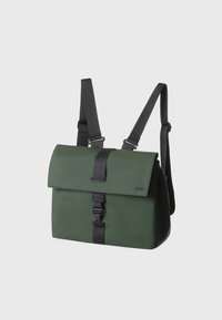 Zaino impermeabile verde con chiusura a pattina, spallacci neri regolabili e una fibbia frontale. Texture liscia e branding minimale sul lato.