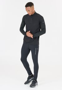 Svart långärmad träningströja med halvdragkedja, tillsammans med svarta leggings som har en reflexdetalj med texten "ENDURANCE". Texturerade accentärmar.