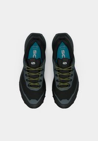 Zapatillas deportivas en negro y gris con suelas de goma texturizadas, cordones verdes y una plantilla azul. Cuentan con una parte superior suave y un collar acolchado.