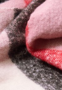 Uldtæppe med en hyggelig blanding af pink, grå og røde nuancer; blød tekstur med et ternet mønster og fleece-finish.