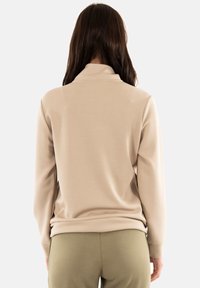 Top beige de manga larga con cuello alto, textura suave y corte relajado, combinado con leggings verde oliva de estilo ceñido.
