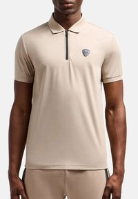 Polo beige con maniche corte, colletto con zip e logo EA7. Realizzato in tessuto liscio con una vestibilità aderente e dettagli minimi.