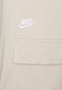 Beige sweatshirt featuring a white embroidered Nike logo and a front pocket. The fabric has a soft, textured finish.