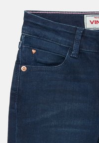 Jeans en denim bleu foncé avec rivets en forme de cœur cuivrés, design classique à cinq poches et détails de couture subtils à la taille.