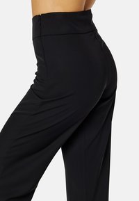 Černé kalhoty s vysokým pasem vyrobené z hladké, texturované látky. Obsahují boční zip a mají upravený střih, který zdůrazňuje moderní design.