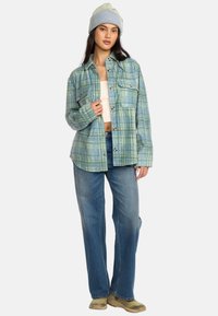 Lyseblå ternet oversized flannel skjorte med knaplukning, to brystlommer, parret med løse denimjeans og en stribet hue.