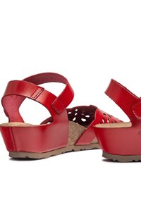 Red leather wedge sandals with a perforated design, adjustable ankle strap, and cork footbed. Textured rubber outsole for grip.