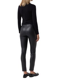 Schwarze, enganliegende Lederhose mit glatter Textur und Nahtdetails, kombiniert mit einem schwarzen Langarmoberteil und schwarzen flachen Schuhen.