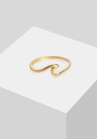 Sottile anello d'oro con un design a onde lisce, posato su una superficie bianca inclinata.