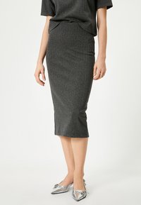 Jupe crayon à rayures gris en tissu texturé, longueur genoux, associée à des chaussures argentées brillantes à bouts pointus avec des accents floraux.