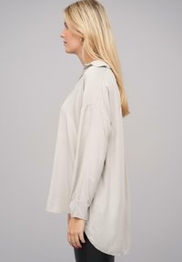Camicia a maniche lunghe grigia chiaro con taglio rilassato, dotata di colletto, orlo arrotondato e polsini elasticizzati. Tessuto morbido.