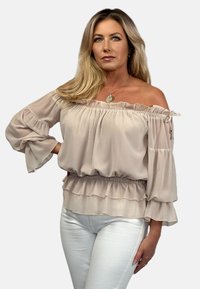 Bluzka bez ramiączek w jasnym beżowym kolorze, z falbanami na rękawach i u dołu, wykonana z przezroczystego materiału, z elastyczną talią i regulowanymi trokami.