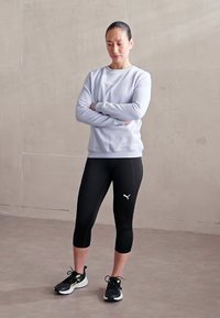 Sportoutfit mit einem hellgrauen Sweatshirt und schwarzen Capri-Leggings, auf denen das Puma-Logo zu sehen ist, kombiniert mit schwarzen Laufschuhen.