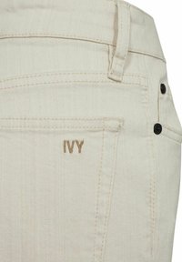 Beige džinsa šorti ar mazu "IVY" logo gaiši brūnā diegā, klasiskā piecu kabatu dizainā un melnas pogas.