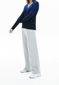 Marinblå och blå v-ringad tröja med långa ärmar, tillsammans med ljusgråa sweatpants. Tröjan har en slim fit och mjuk textur.