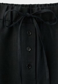 Pantalon en lin noir avec taille élastique, cordon de serrage et trois boutons noirs sur le rabat de braguette avant.