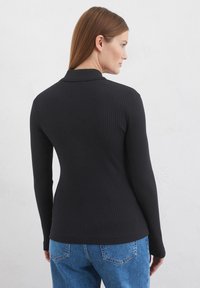 Schwarzes, geripptes Langarmoberteil mit Kragen, tailliertem Schnitt und glatter Textur, kombiniert mit blauen, hoch taillierten Jeans mit sichtbaren Nähten.