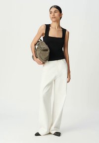 Black fitted tank top, white wide-leg pants, and black pointy-toed shoes. Carrying a textured, earthy-toned slouchy handbag.