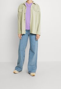 Jasnozielona koszula z sztruksu, fioletowy T-shirt i dżinsy o szerokich nogawkach w kolorze niebieskim, w połączeniu z trampkami z żółtymi akcentami.