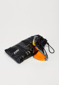 Sort polstrede etui med snor, der indeholder sporty solbriller med transparent ramme og orange tonede linser.