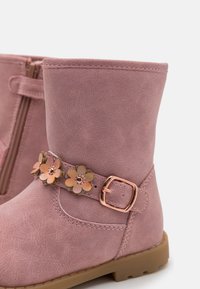 Pink synthetic boots with a textured finish, featuring a floral accent strap with metallic details and side zipper closure.