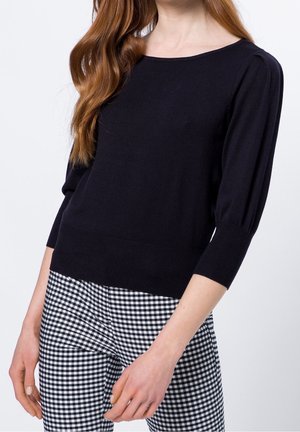Maglione blu navy con maniche a palloncino a tre quarti, orlo a costine e texture a maglia morbida, abbinato a pantaloni a quadri in bianco e nero.