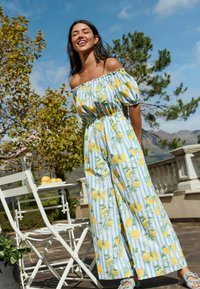 Off-the-shoulder jumpsuit in blue and white stripes, featuring a lemon pattern. Elastic waistband and puffed sleeves. Textured fabric.