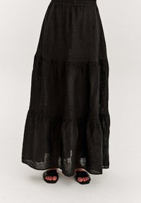 Čierna maxi sukňa z ľanu s vrstveným dizajnom, ktorá sa vyznačuje elastickým pásom a ľahkou, textúrovanou tkaninou. V kombinácii s čiernymi sandálmi.