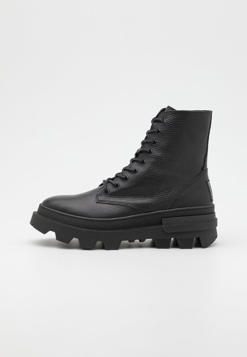 Botte montante en cuir noir avec semelle épaisse crantée texturée et fermeture à lacets sur fond blanc uni.