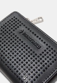 Czarny syntetyczny portfel z teksturowaną powierzchnią z wypukłymi okrągłymi ćwiekami oraz logo. Widoczny zamek błyskawiczny z boku.