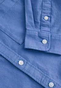 Camicia di cotone azzurro chiaro con design a bottoni sul fronte, bottoni bianchi, colletto a punta e cuciture ben rifinite.