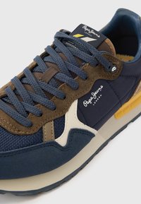 Ναυτικό μπλε και καφέ αθλητικό παπούτσι με σουέτ και διχτυωτά υλικά, στρογγυλή μύτη, αντίθετε�ς λεπτομέρειες και υφασμένα κορδόνια με λογότυπο στη πλευρά.