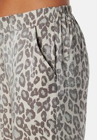 Luipaardprintbroek met een zacht, glanzend materiaal, voorzien van plooien en een elastische tailleband voor comfort. Kleurenpalet omvat beige en grijs.