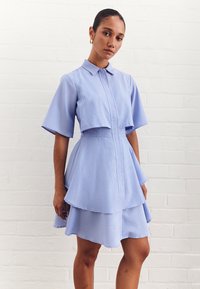 Gestreiftes blaues Hemdkleid mit kurzen Ärmeln, Knopfverschluss vorne und geschichtetem Saum. Hergestellt aus glattem Stoff mit strukturiertem Design und Kragen.