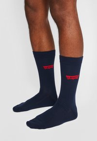 Tamno plave pamučne čarape s rebrastim rubom i crvenim "Levi's" logom na zapešću. Glatka tekstura s prilagođenim oblikom.