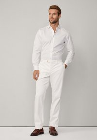 Camicia bianca a maniche lunghe con chiusura a bottone, abbinata a pantaloni bianchi, completata da mocassini in pelle marrone. Design semplice e sartoriale.