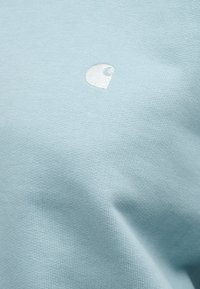 Ανοιχτό μπλε βαμβακερό μπλουζάκι με μαλακή υφή, που διαθέτει ένα μικρό λευκό κεντημένο λογότυπο στην αριστερή πλευρά.