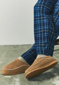 Pruunist nubukist libisemisega kingad dekoratiivse õmblus�äärega, millele on sobitatud tumesinised ruudulised püksid, millel on heledast ruudustikust muster.