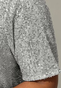 Top plateado con lentejuelas y mangas cortas, que presenta una superficie texturizada con lentejuelas reflectantes que crean un diseño patternado.