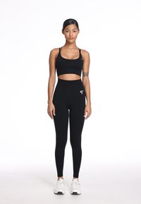 Zwarte sportieve crop top en high-waisted leggings, beide aansluitend, gecombineerd met witte sneakers. Heeft minimale branding en een gladde textuur.