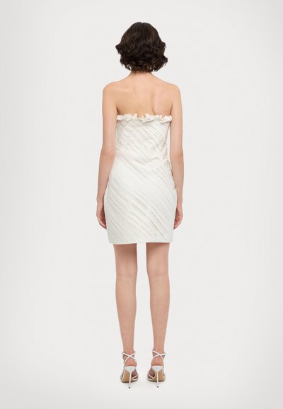 Strapless witte jurk met een geplooid ontwerp, bloemenrand en een aansluitende silhouet. Gecombineerd met witte, bandjes sandalen met hoge hakken.