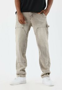 Pantalones cargo beige con bolsillos con solapa, acentos de botones y un ajuste relajado. Combinados con zapatillas blancas, que presentan una textura de denim deslavado.