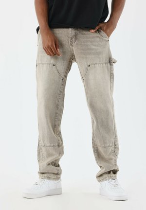 Pantalones cargo beige con bolsillos con solapa, acentos de botones y un ajuste relajado. Combinados con zapatillas blancas, que presentan una textura de denim deslavado.