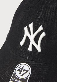 Gorra de béisbol negra hecha de tela, con un logo bordado en blanco de los New York Yankees. Incluye una etiqueta redonda '47 Clean Up'.