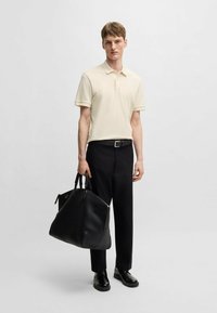 Polo shirt beige a maniche corte, pantaloni neri e scarpe nere lucide. Tiene una grande borsa a tracolla in pelle nera con manici doppi.