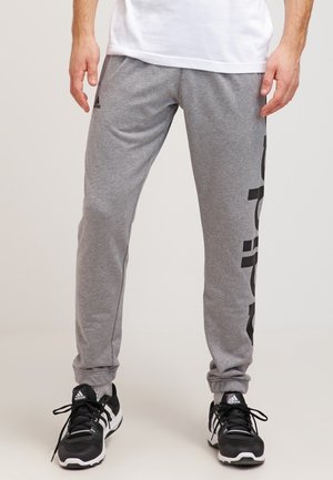 Graue Baumwoll-Sweatpants mit schwarzen Grafiken entlang der linken Seite. Verfügt über eine lockere Passform und elastische Bündchen. Tragen mit schwarzen Sportschuhen.