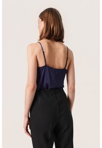 Navy satin camisole with thin adjustable straps, paired with high-waisted black trousers. Smooth texture and simple design.