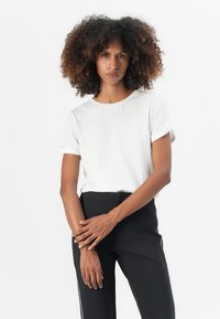 White short-sleeve t-shirt with rolled cuffs, round neckline, and smooth texture, paired with black pants featuring side stripes.